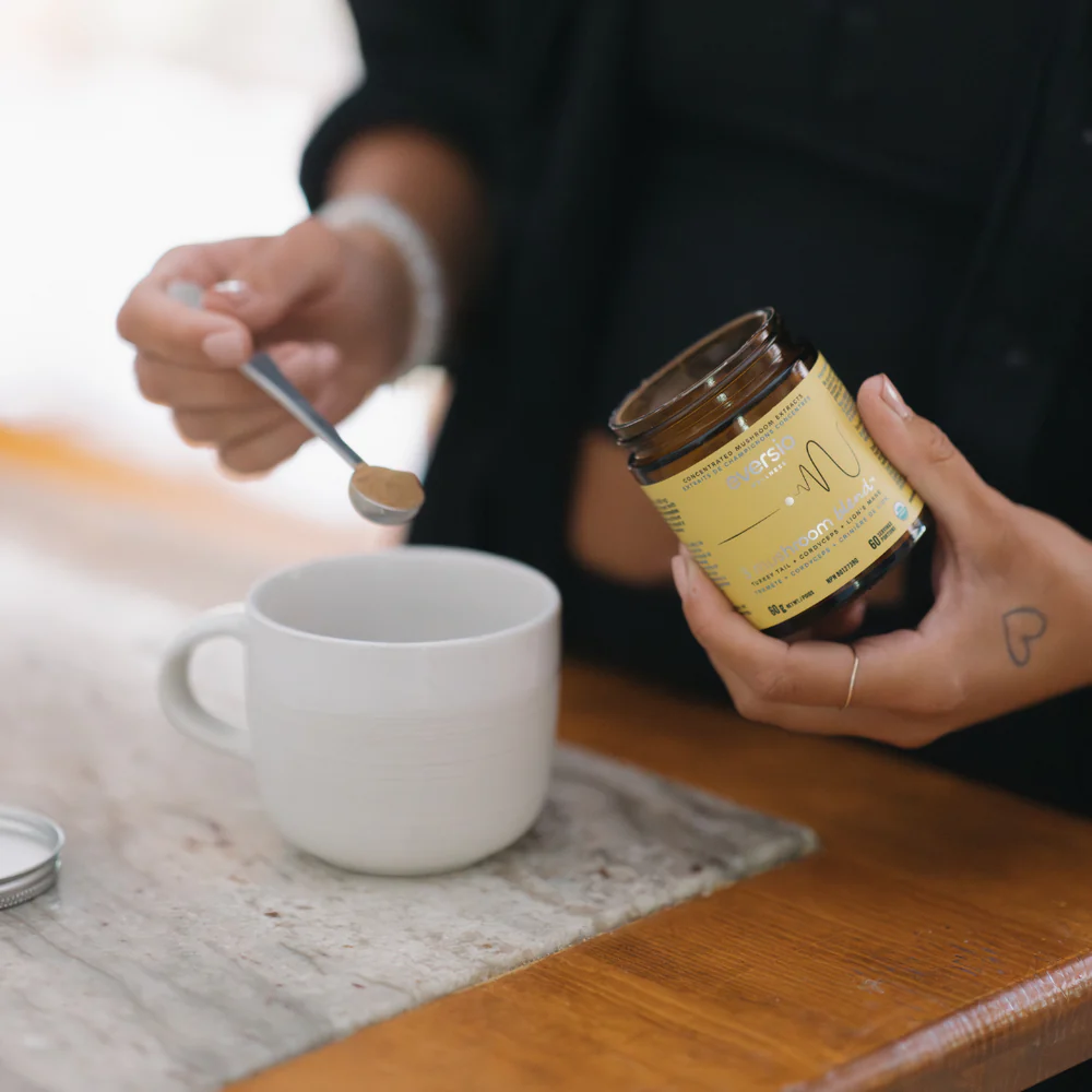 A spoon measuring out lions mane extract powder next to a cup of coffee